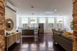 A spacious kitchen with a central island, large windows, and a dining area with a sofa and chairs. - NEW | Beautifully Restored Historic Apartment (Willemstad)