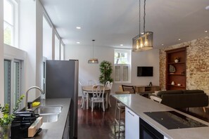 Une cuisine moderne avec un coin repas, un îlot central intégré et un espace de vie agrémenté d’un mur en briques apparentes.