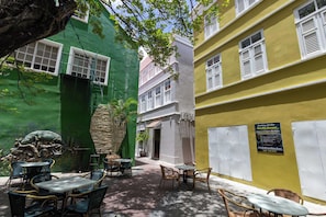 A courtyard with outdoor seating, a green wall with a cactus sculpture, and a building with a yellow facade. - NEW | Beautifully Restored Historic Apartment (Willemstad)