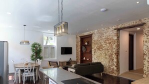 Eine moderne Küche mit einer zentralen Kochinsel, Essbereich mit Stühlen, einer Pendelleuchte und einer Wand in Backsteinoptik.