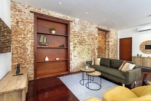 Ein Wohnzimmer mit Backsteinwand, Holztür, einer Couch, einem Couchtisch und einem kleinen Beistelltisch.
