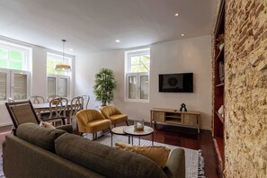Ein Wohnzimmer mit einer Sofagarnitur, einem Essbereich mit Stühlen und einem Tisch, einer Topfpflanze, einem an der Wand befestigten Fernseher und einer Steinwand.