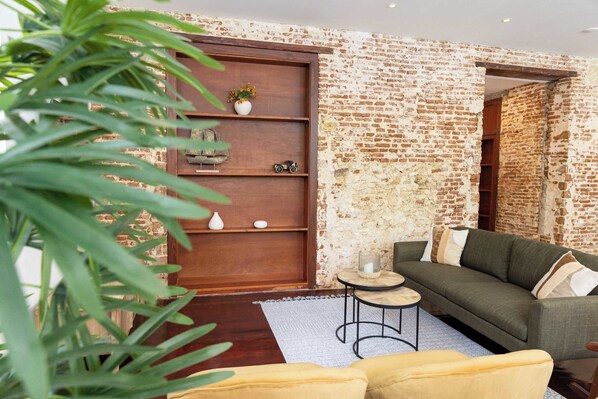 Un salón acogedor con pared de ladrillo, estantería de madera, sofá verde y sillón amarillo.