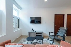 A modern living room with a flat-screen TV mounted on the wall, a grey entertainment unit, a round coffee table, a grey office chair, and a pink sofa. - Elegant Apartment in Historic Punda (Willemstad)