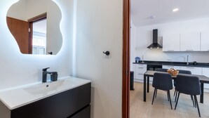 A modern kitchen with white cabinets, a black countertop, and a dining area with two chairs. - Elegant Apartment in Historic Punda (Willemstad)