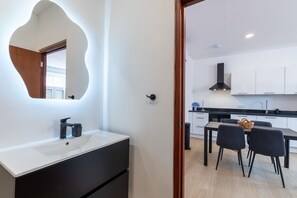 A modern kitchen with white cabinets, a black countertop, and a dining area with two chairs. - Elegant Apartment in Historic Punda (Willemstad)