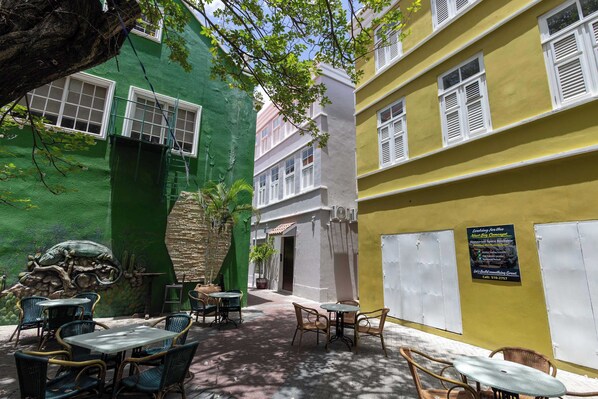 A courtyard with outdoor seating, a green wall with a cactus sculpture, and a building with a yellow facade. - Elegant Apartment in Historic Punda (Willemstad)