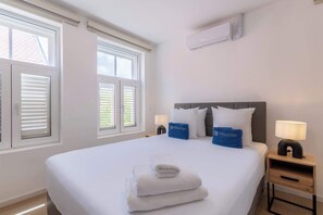 Una habitación de hotel con una cama grande, dos mesitas de noche, una ventana con persianas y un equipo de aire acondicionado en la pared.