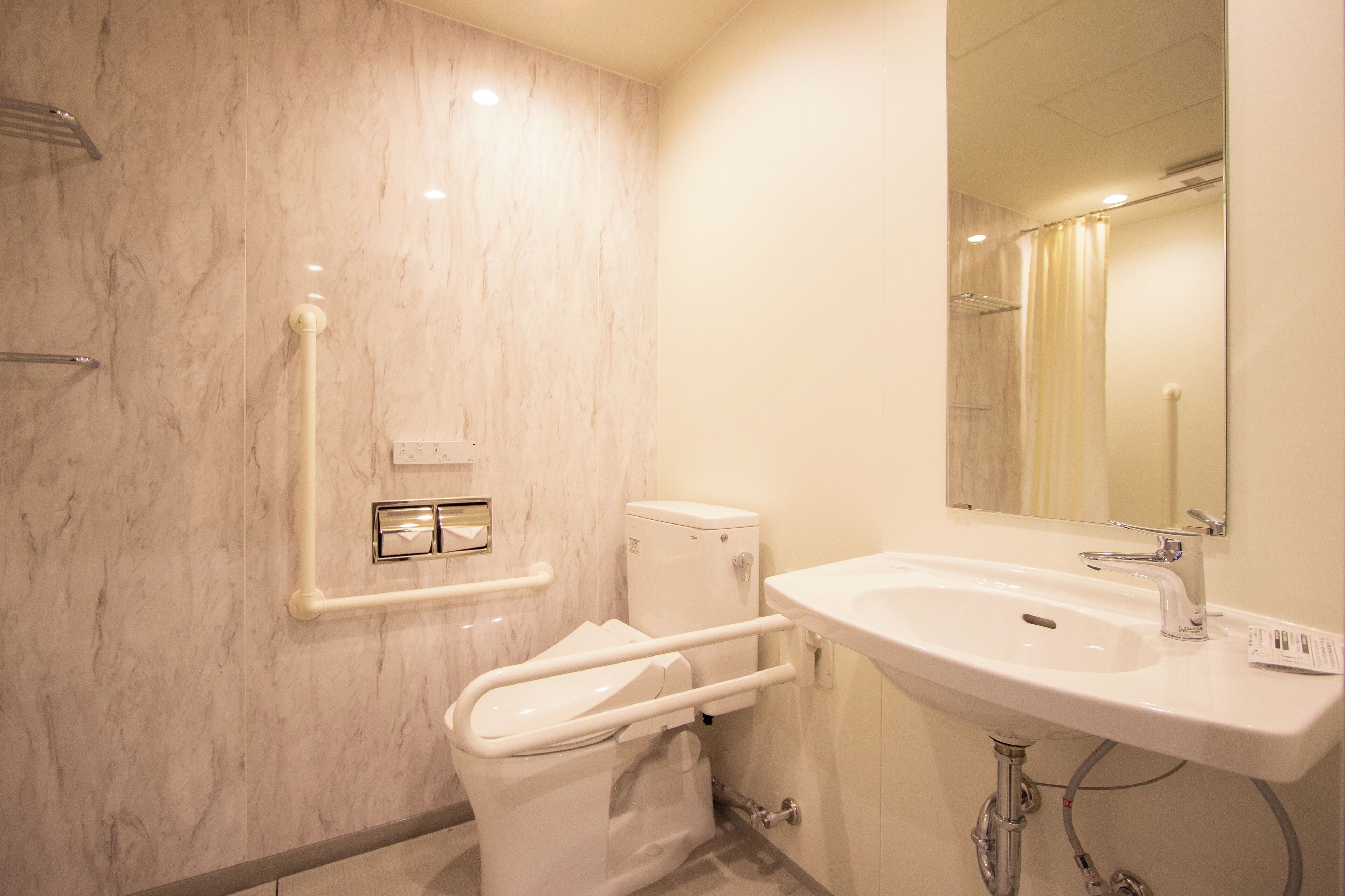 A modern bathroom with a marble wall, a white sink, and a toilet with a grab bar.