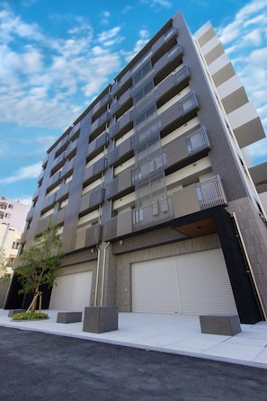 A multi-story building with a modern architectural design, featuring balconies on each floor and a garage door at the base.