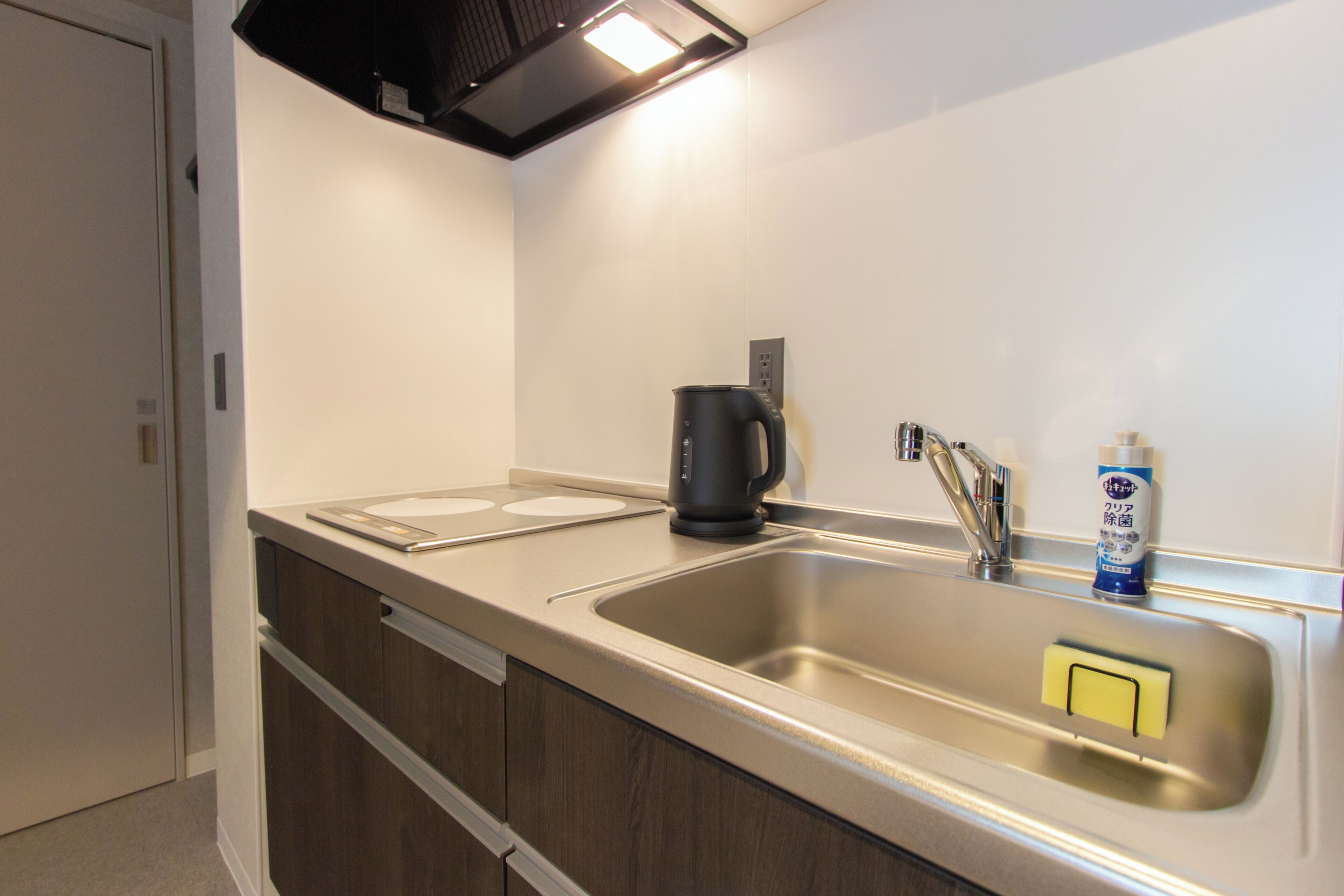 A kitchen with a stainless steel sink, a coffee maker, and a bottle of dish soap.