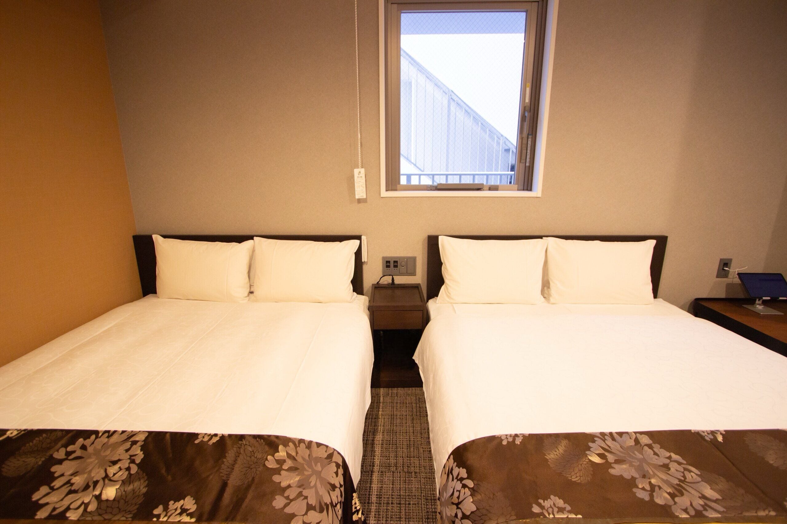 Een hotelkamer met twee bedden, een raam en een nachtkastje met een lamp.