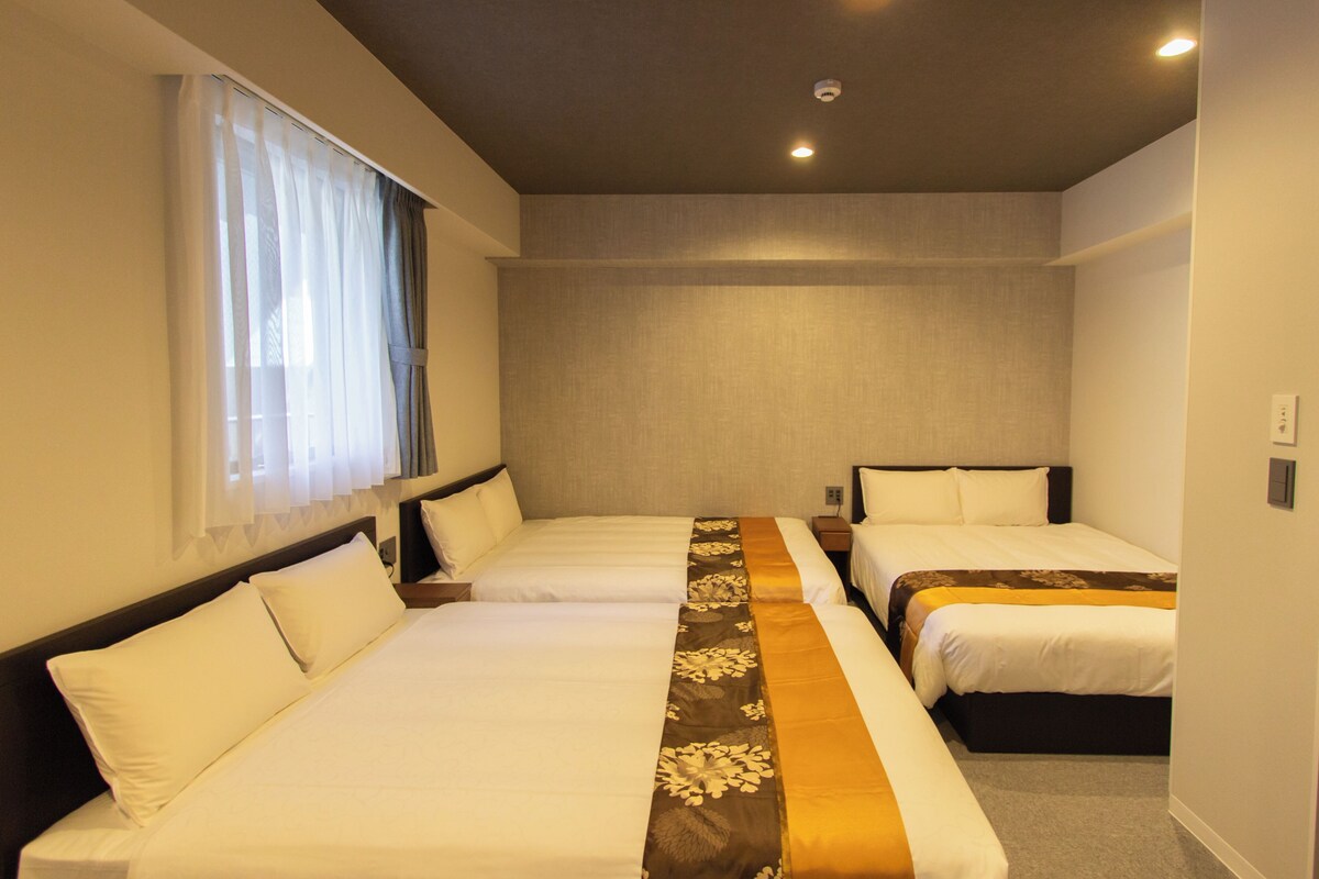 A hotel room with two beds, a window with sheer curtains, and a ceiling light.