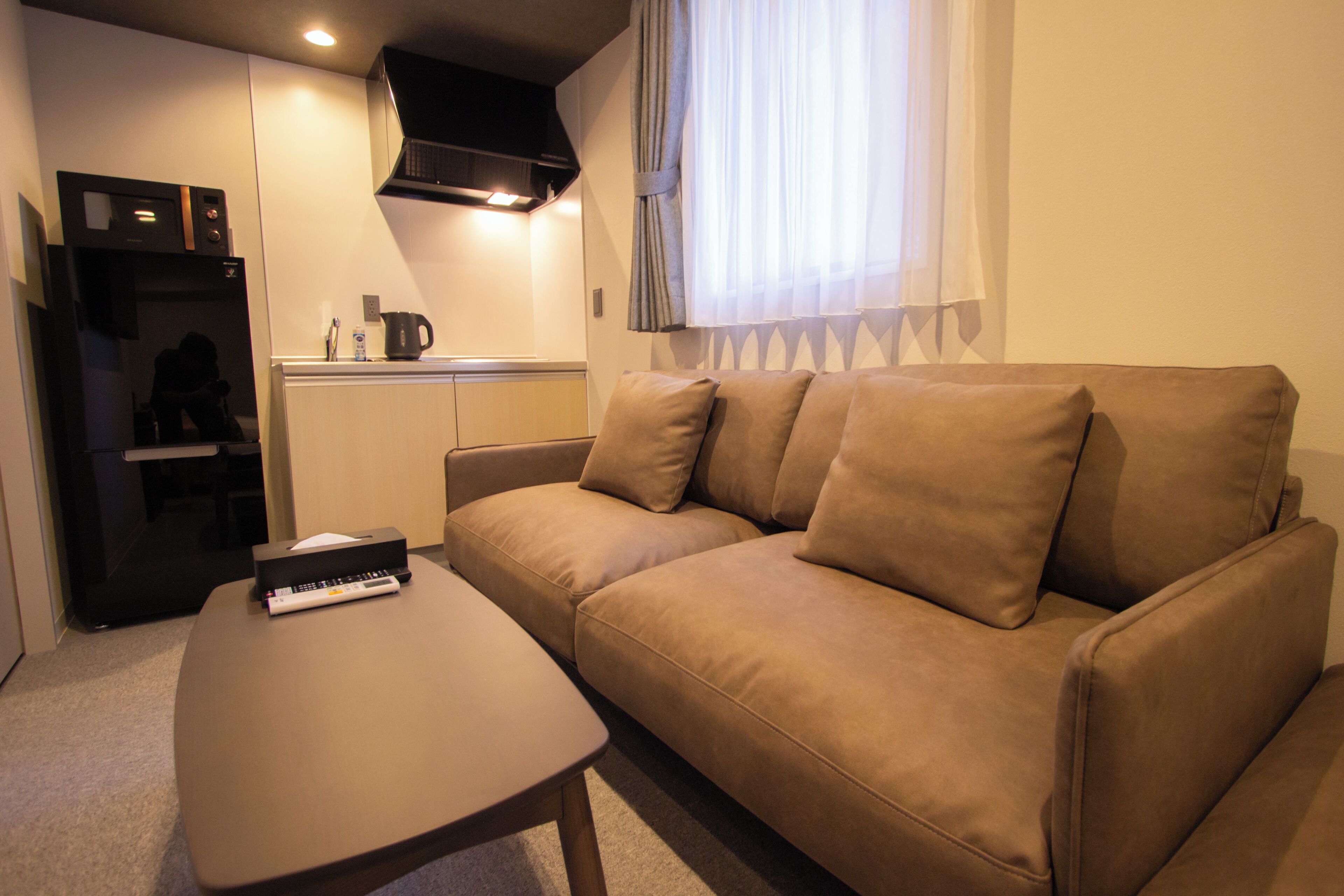 A compact living space with a sofa, a coffee table, a kitchenette, and a TV.