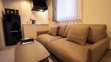 A compact living space with a sofa, a coffee table, a kitchenette, and a TV.