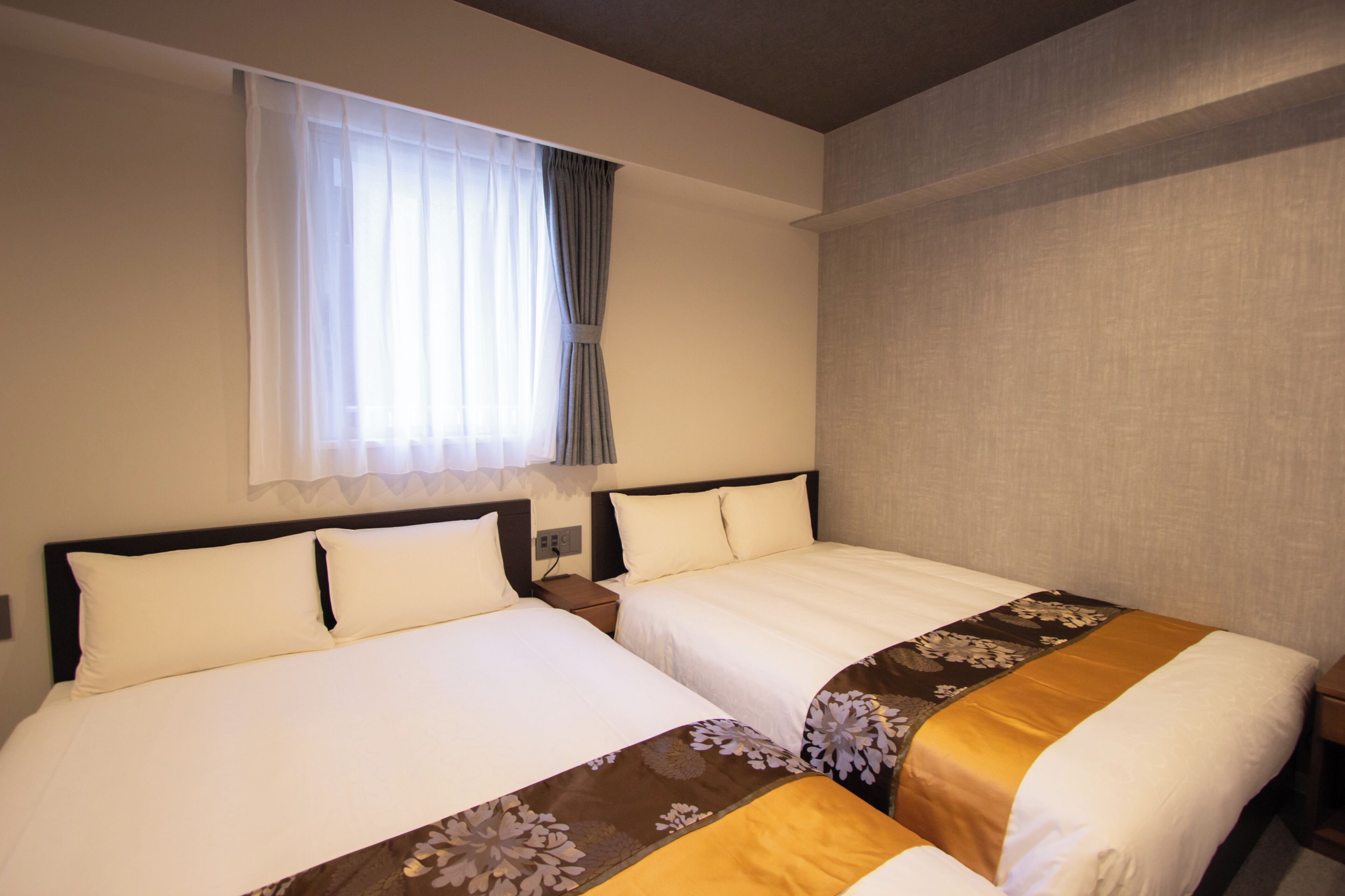 Habitación de hotel con dos camas, una ventana con cortinas y una pared lisa.
