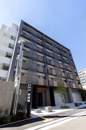 Um edifício moderno de vários andares com fachada plana, janelas grandes e uma entrada visível com moldura preta.