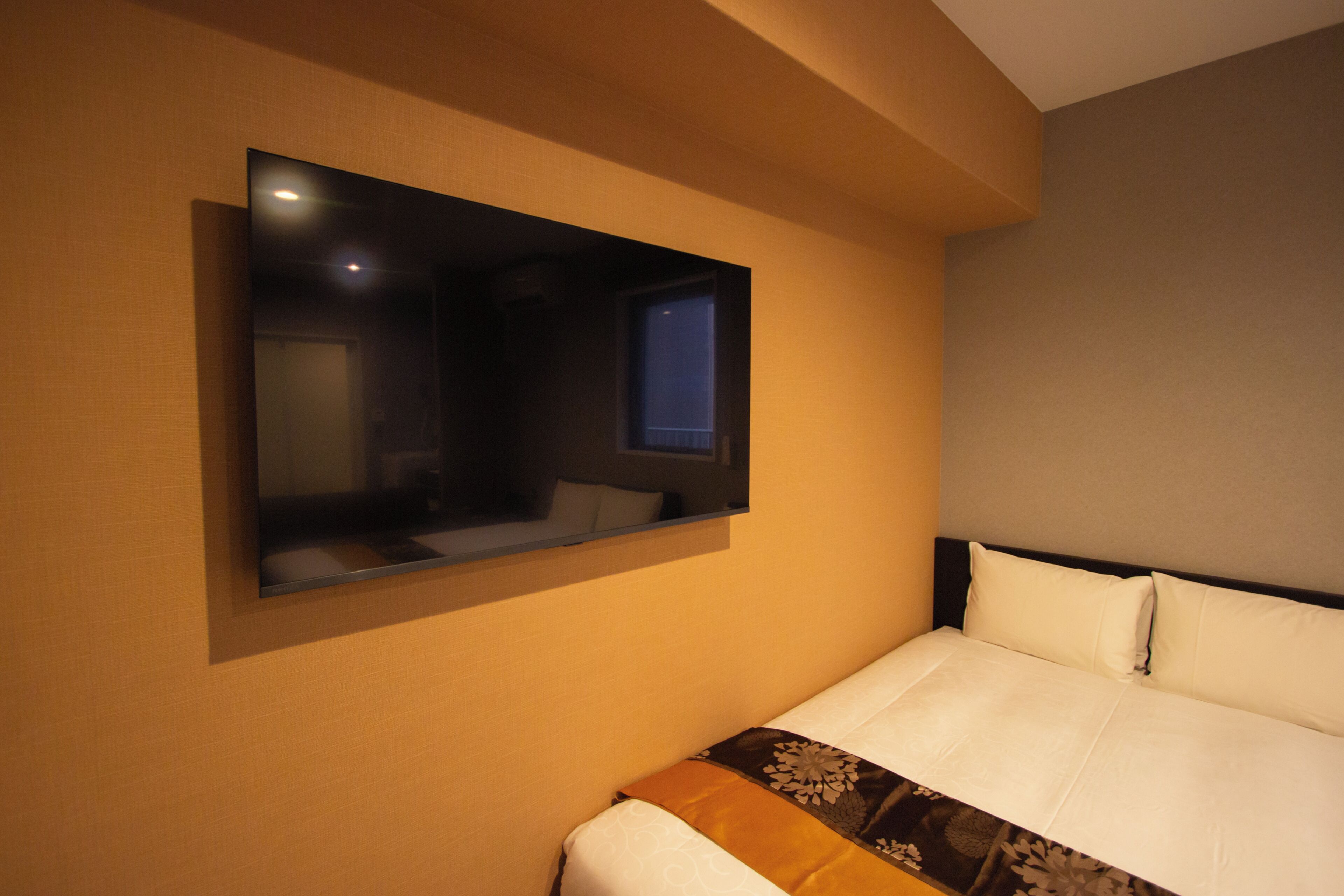 Una habitación de hotel con cama, televisor montado en la pared y ventana.