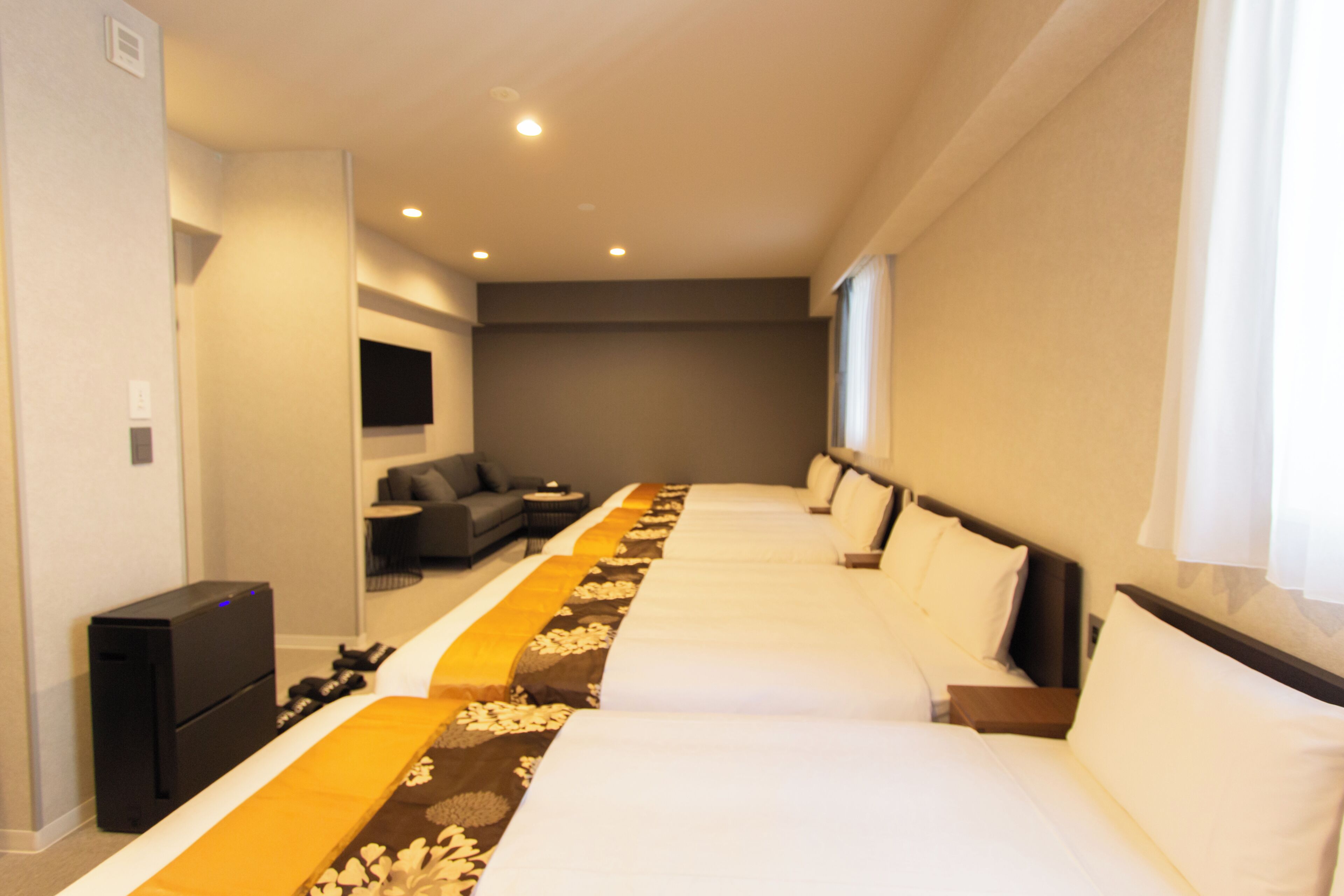 A hotel room with two beds, a sofa, a TV, and a desk.