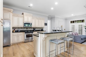 A modern kitchen with white cabinetry, stainless steel appliances, and a central island with bar stools. - Villa Bella - Luxury 4BR Home w/ Secluded Private Pool (Sleeps 16) (North Myrtle Beach)