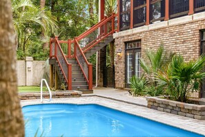 A swimming pool with a red staircase leading to a building, surrounded by greenery. - Villa Bella - Luxury 4BR Home w/ Secluded Private Pool (Sleeps 16) (North Myrtle Beach)
