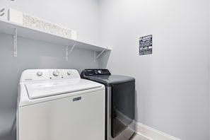 A laundry room with a Maytag washer and dryer, a white shelf above the dryer, and a laundry rules sign on the wall. - Villa Bella - Luxury 4BR Home w/ Secluded Private Pool (Sleeps 16) (North Myrtle Beach)