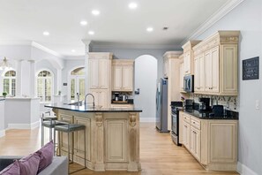 A spacious kitchen with a central island, built-in appliances, and a view to the dining area. - Villa Bella - Luxury 4BR Home w/ Secluded Private Pool (Sleeps 16) (North Myrtle Beach)