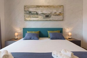 Ein Hotelzimmer mit einem großen Bett, zwei Nachttischen mit Lampen und einem an der Wand hängenden abstrakten Gemälde.