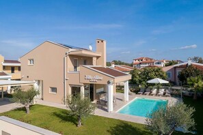 Eine Villa mit Pool, Sitzgelegenheiten im Freien und einer überdachten Terrasse.