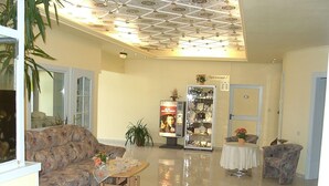 Un hall d’entrée spacieux avec un plafond haut, un coin salon avec un canapé et des fauteuils, une petite table ornée d’un vase de fleurs et une vitrine contenant divers objets.