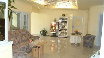 Een ruime lobby met een hoge plafond, een zithoek met een bank en fauteuils, een kleine tafel met een bloemenvaas, en een display met objecten.