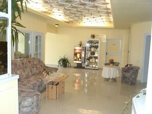 Un vestíbulo amplio con techo alto, una zona de estar con sofá y sillones, una pequeña mesa con un jarrón de flores y una vitrina con objetos.