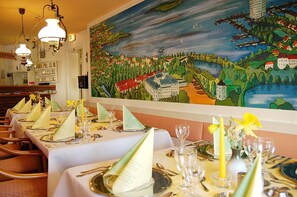 Un restaurante con mesas dispuestas para comer, un gran mural en la pared y vistas al mar.
