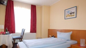 Une chambre d’hôtel avec un lit, un bureau avec une chaise, une table avec une bouteille et un tableau au mur.