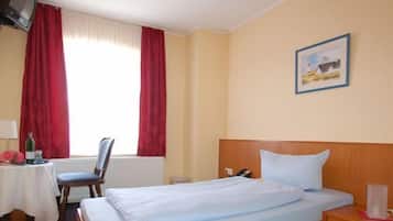 Een hotelkamer met een bed, een bureau met een stoel, een tafel met een fles en een schilderij aan de muur.