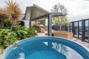 Piscina en la azotea con pérgola, abundante vegetación y vista a la ciudad.