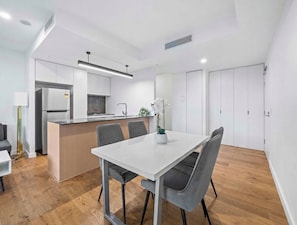 Eine moderne Küche mit einer zentralen Kochinsel, einem Essbereich mit weißem Tisch und grauen Stühlen sowie einem Holzboden.