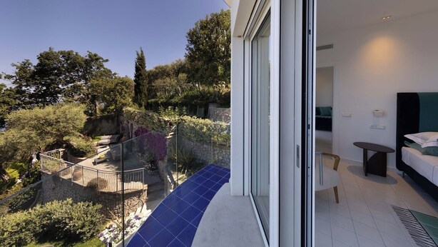 Ein modernes Hotelzimmer mit einem Balkon, der einen angelegten Garten und Bäume blickt.