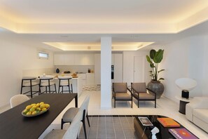 A modern kitchen with white cabinets, a dining area with a black table, and a living space with a sofa and a large plant. - Villa Baia Serena, Panorama with Private Pool (Massa Lubrense)