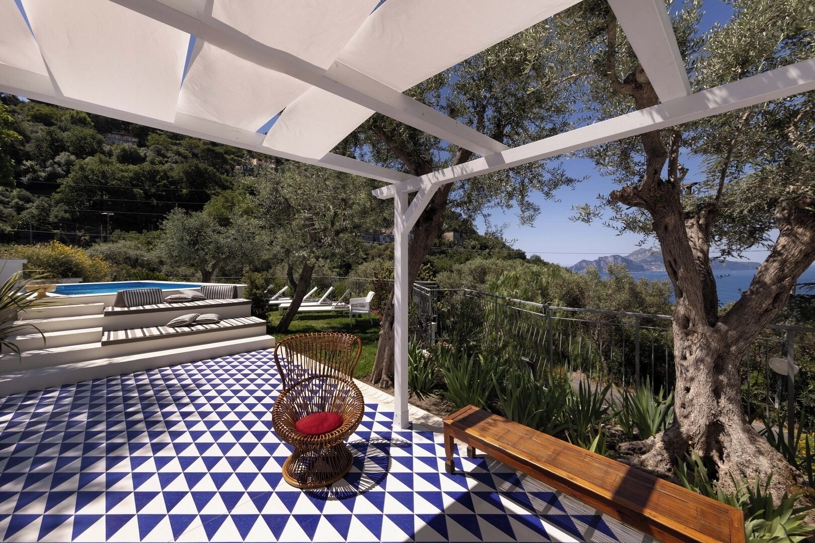 A covered outdoor area with a patterned floor, lounge chairs, and a view of the sea.