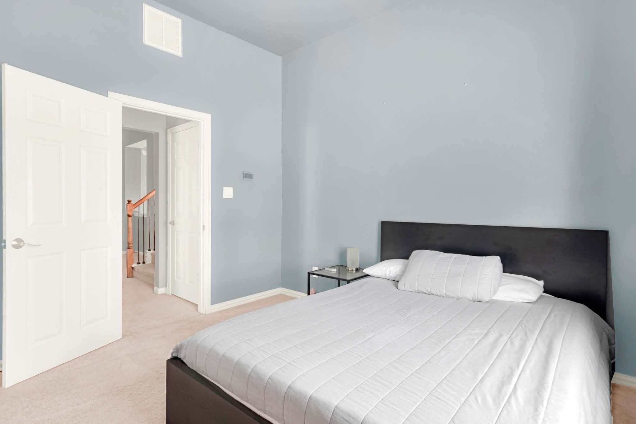Une chambre à coucher comprenant un lit, une table de chevet, une lampe et une porte donnant sur une autre pièce.