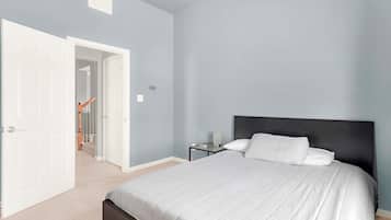 Une chambre à coucher comprenant un lit, une table de chevet, une lampe et une porte donnant sur une autre pièce.