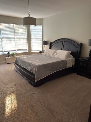 A bedroom with a bed, a nightstand, a lamp, and a window with blinds.