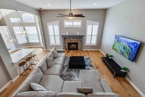 A modern living room with a sectional sofa, a fireplace, a flat-screen TV, and a dining area with bar stools.