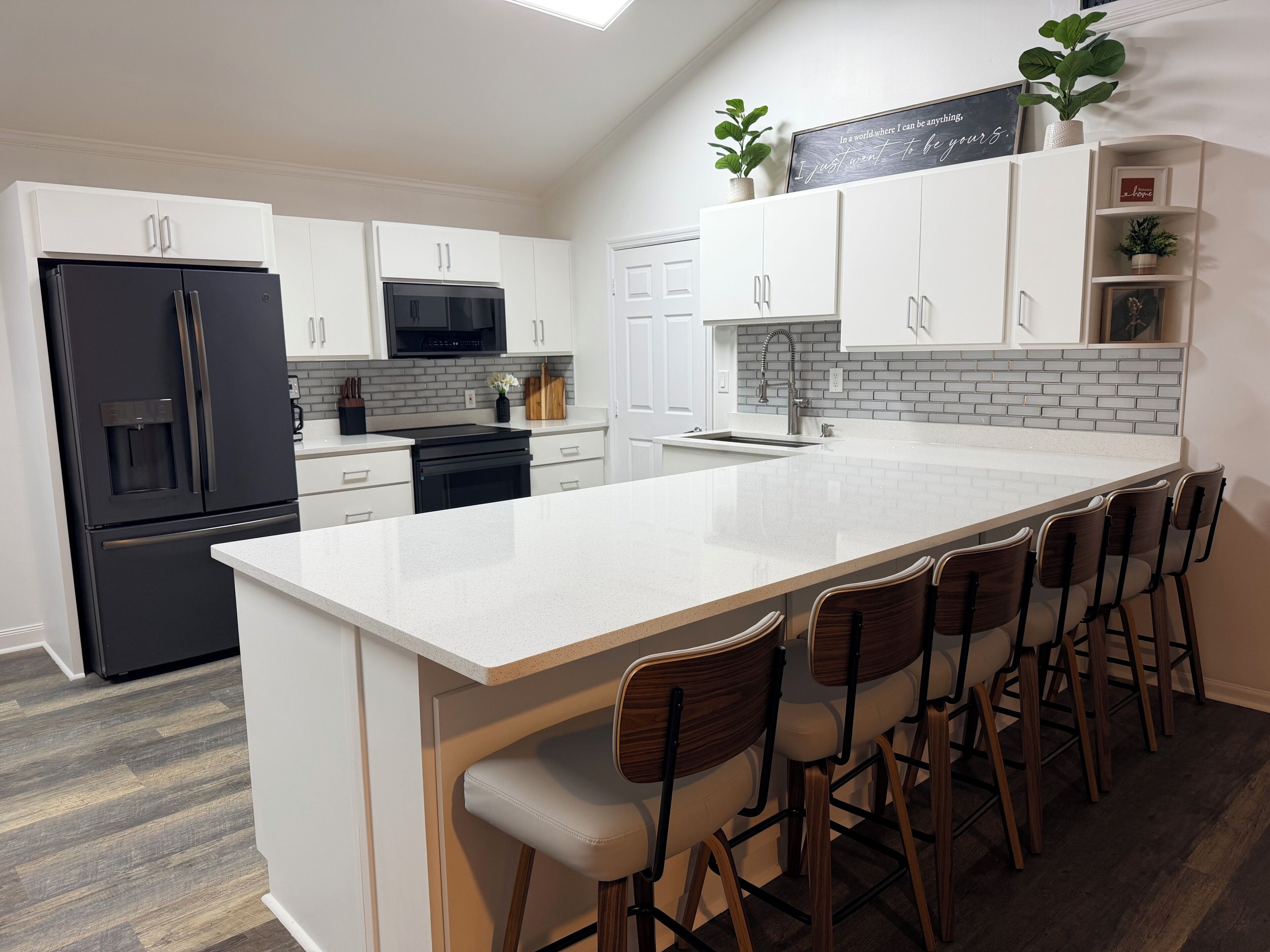 A modern kitchen with white cabinetry, a black refrigerator, a stainless steel range, and a bar area with stools.
