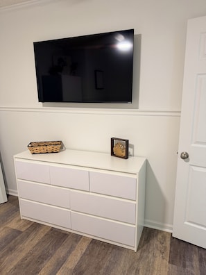 Un aparador blanco con cajones, un televisor de pantalla plana montado en la pared de arriba y una puerta a la derecha.