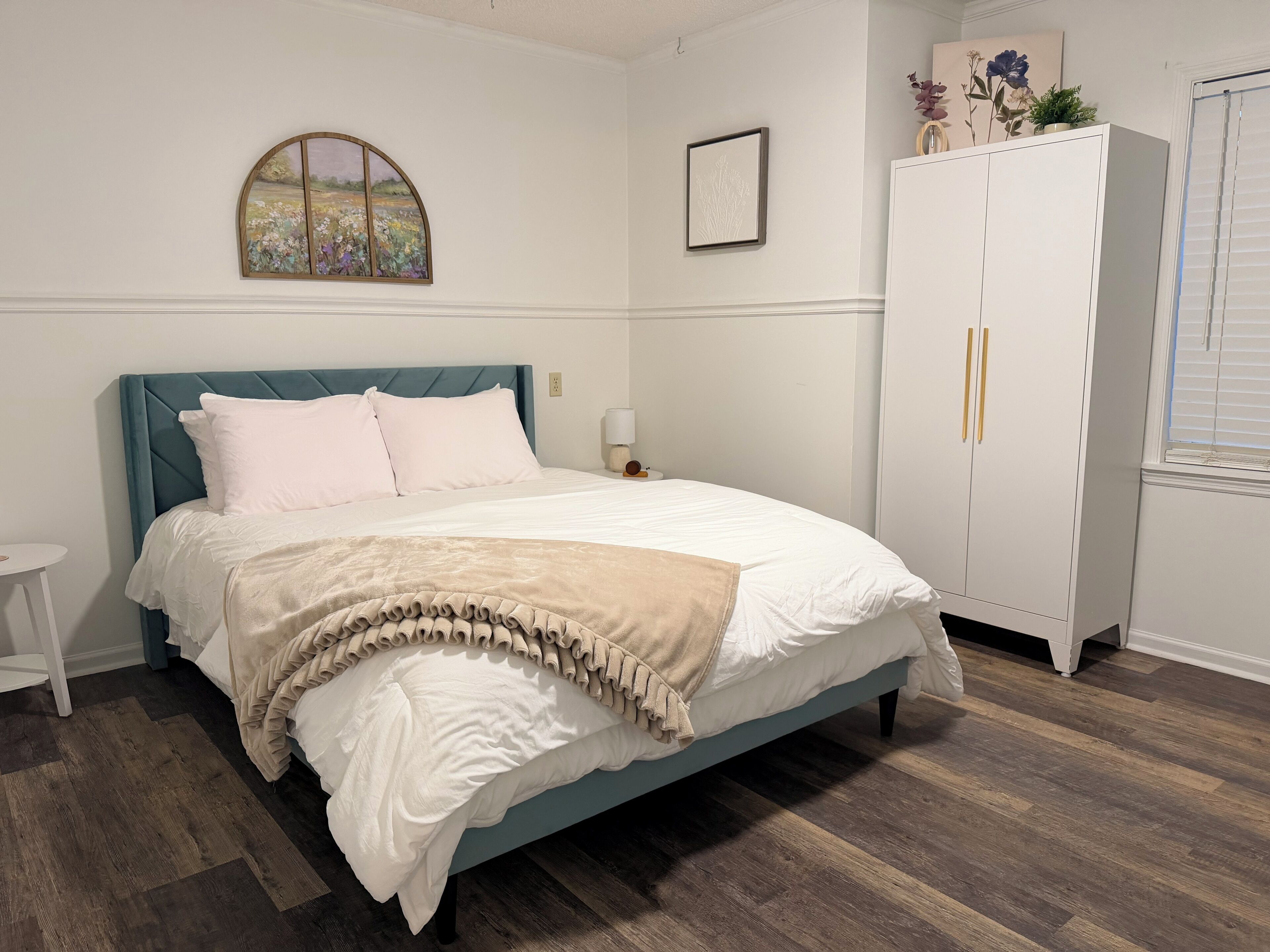 A bedroom with a bed, a nightstand, a wardrobe, and a painting on the wall.