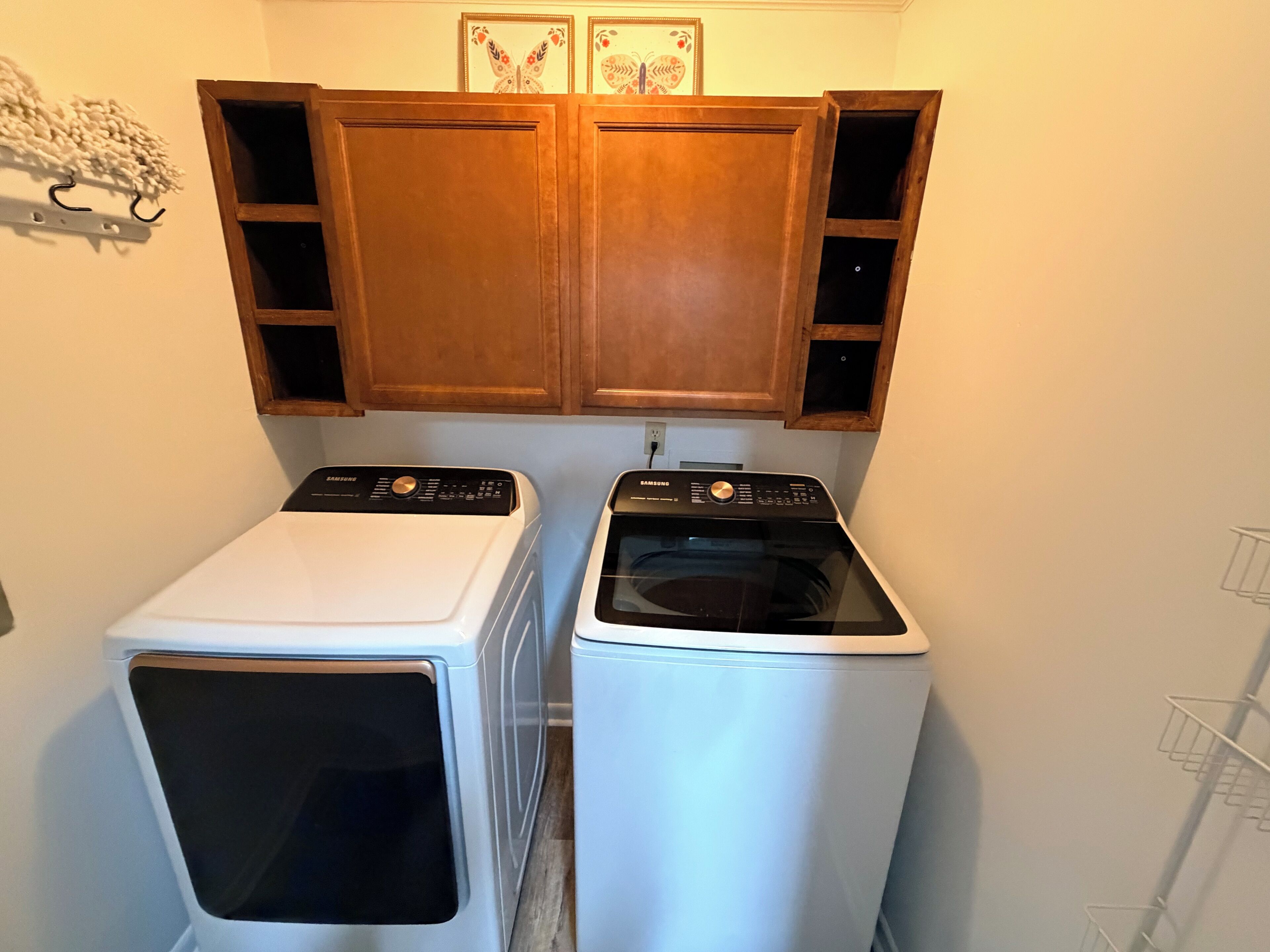 A laundry area with two washing machines, wooden cabinets above, and a white wall.