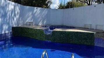 A swimming pool with a clear blue water surface, surrounded by a white wall and a hedge.