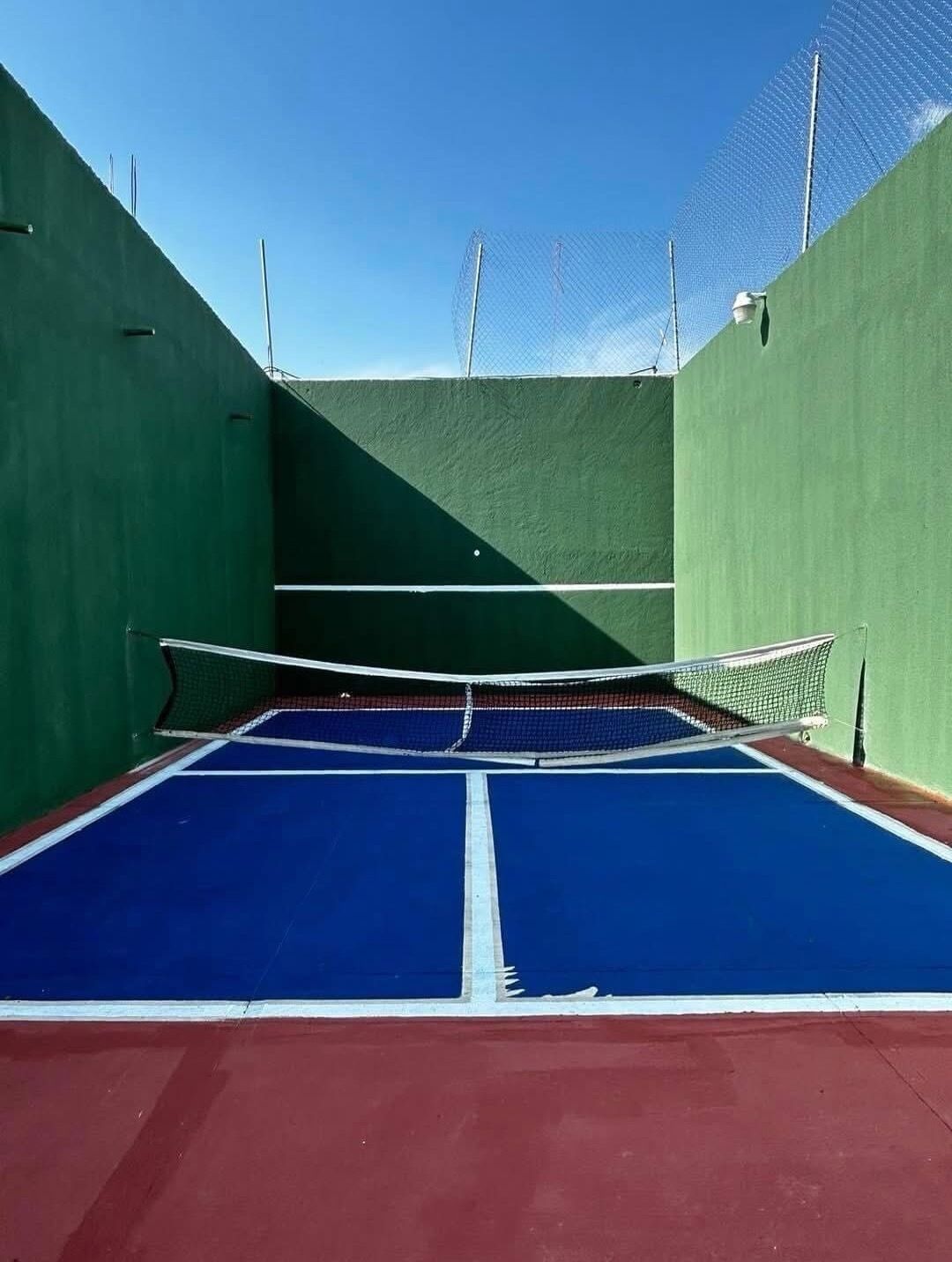 Un court de tennis intérieur doté d’un filet, de murs verts et d’une surface de jeu bleue.